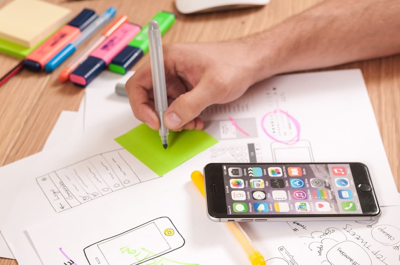 Mão desenhando um wireframe a lápis, com um celular sobre o papel